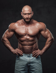 Fototapeta na wymiar Powerful and handsome bodybuilder with hairless head poses in dark background with naked torso with angry face looking at camera.
