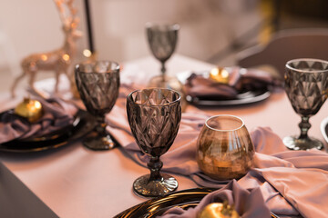 Close up of festive Christmas table setting with empty wine glasses and black plate with gold garnet