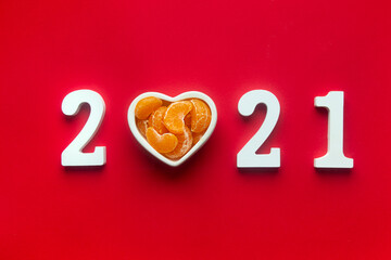 on a red background white numbers 2021. instead of the number 0, a plate in the shape of a heart with slices of tangerines.