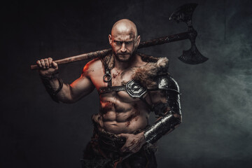 Violent scandinavian barbarian with muscular nude build and bald head posing in dark atmospheric background with smoke with his huge two handed axe.