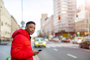 Young black man using phone and waiting for a taxi
