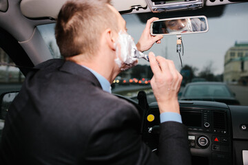 Businessman shaving in car by razor and foam at the wheel. Shaving man in the driver's seat....