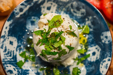 Fototapeta na wymiar Delicious burrata with fresh basil leaves and italian olive oil. Served in a blue plate. From Apulia region in Italy. Professional macro food top view photography.