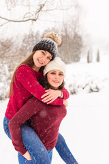 TWO GIRLS IN RED SWEATERS IN THE WINTER FOREST. THE SISTERS WALK IN THE SNOW IN THE PARK