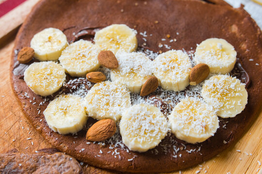 Sliced banana with almonds and coconut powder on oat chocolate or cacao homemade crepe. Adapted for a sports diet. Top view food close up.