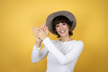 Young caucasian woman wearing hat over isolated yellow background clapping and applauding happy and joyful, smiling proud hands together