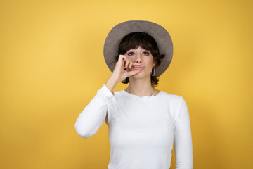 Young caucasian woman wearing hat over isolated yellow background mouth and lips shut as zip with fingers. Secret and silent, taboo talking