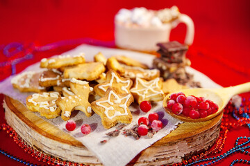 Christmas gingerbread cookies, chocolate and frozen berries, on a wooden stand, a cup of hot chocolate with marshmallows in the back, red background. Christmas and New Year concept.