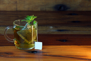 cup of mint tea on a wooden table with mint leaves around and infusion into the cup