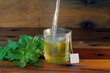 cup of mint tea on a wooden table with mint leaves around and infusion into the cup © Charles Belmon 