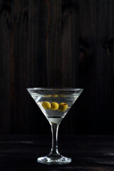 Martini glass with cocktail and olives on black background. Cocktail Margarita with olive and ice on the wooden table. copy space. alcohol drinks. vertical