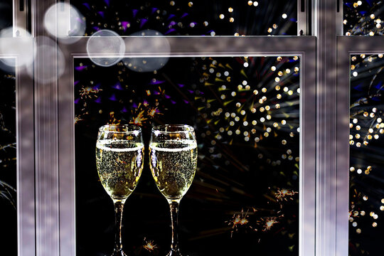 Two glasses of champagne on windowsill against firework display background. New Year's background.