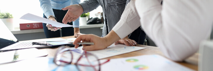 Office workers standing by the table with laptop and papers and discussing new business project