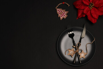 New Year and Christmas table setting. Modern and elegant. Black plate, gold cutlery and Christmas star flower, Poinsettia on a black background. Copy space. flat lay.