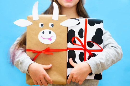 crazy exited happy girl with gifts in the red christmas hat on the blue background with copy space. wrapping paper with cow spots and bull.