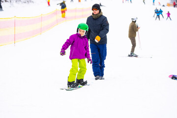 Fototapeta premium Instructors teach a child on a snow slope to snowboard