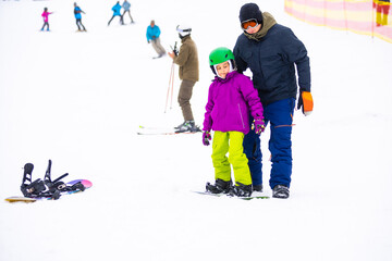 Fototapeta na wymiar At Cold Winder Day at Mountain Ski Resort Father Teaching Little Daughter Snowboarding