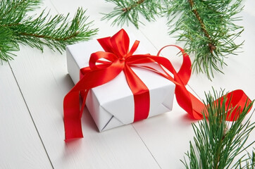 Fototapeta na wymiar Christmas gift box with red ribbon and pine tree branches on white wooden background