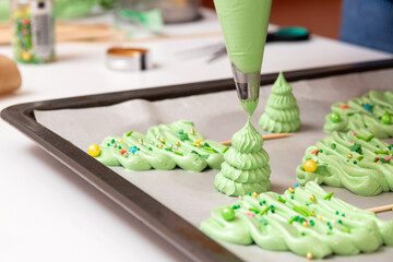 Green meringue in the form of Christmas trees of different shapes on parchment before baking. Selective focus.