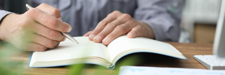 Close up of young man sitting at the table and making notes at work