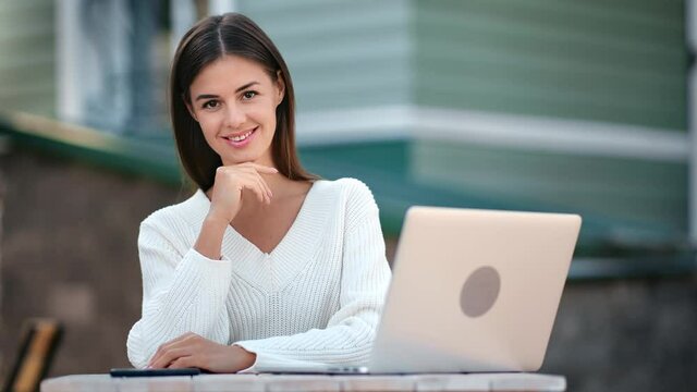 Portrait of smiling female posing at house facade in front of laptop. Medium shot on RED camera