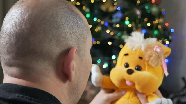 A man holds a teddy bear, near a Christmas tree. freaky people concept. play with a toy. soothing toy for autism