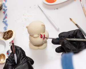 Applying red paint with a brush on the figure of a polar bear made of chocolate. Selective focus.