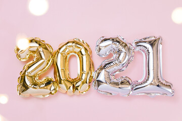 Gold and silver foil balloons numeral 2021 and fairy lights on pastel pink background.