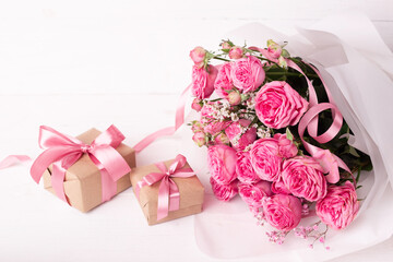 Fresh pastel soft pink roses, and gift boxes wrapped in kraft papper with ribbons on white wooden table.