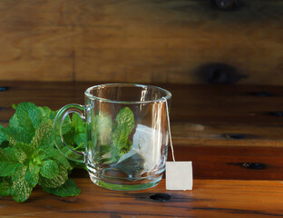 cup of mint tea on a wooden table with mint leaves around and infusion into the cup