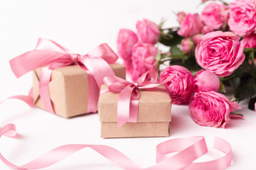Fresh pastel soft pink roses, and gift boxes wrapped in kraft papper with ribbons on white wooden table.