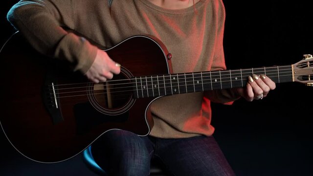 Close up of young woman playing strumming guitar sitting on stool