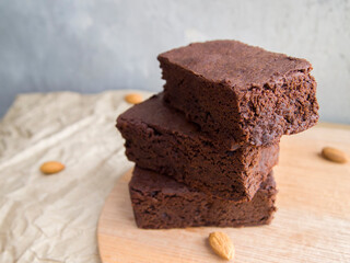 Three pieces of delicious brownie on a beige and gray background. Appetizing chocolate cake with a rich taste. Next to the cake are nuts (almonds). Yummy dessert.