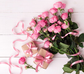 Obraz na płótnie Canvas Fresh pastel soft pink roses, and gift boxes wrapped in kraft papper with ribbons on white wooden table.