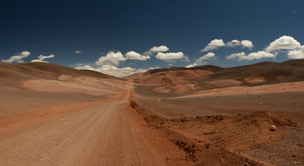 Fototapeta na wymiar The dirt road high in the Andes mountains. Traveling along the route across the arid desert and mountain range. The sand and death valley under a deep blue sky in La Rioja, Argentina. 
