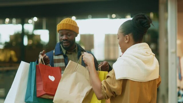 Excited joyful black young couple of stylish people running in hallway of shopping mall with bags enjoying holiday sale shopping on black friday.