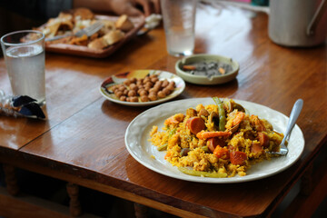 white dish with rice, shrimp, chili, clams and a fork in the table there are also peanuts, cigarettes, glasses
