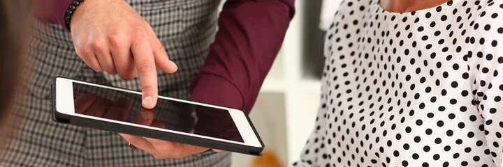 Close up of young man holding electronic pad PC and pointing finger at display while working with colleagues in office