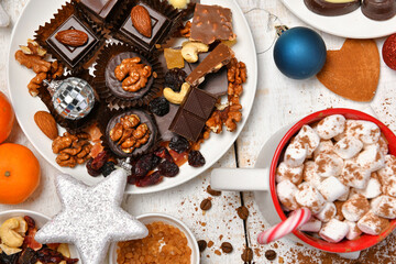 sweet food top view background for merry christmas or new year holiday decoration - chocolate candies, tangerines, cookies, marshmallow and cocoa latte on white wood
