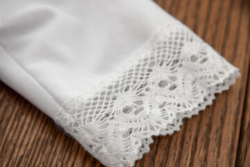 Sleeve of a christening shirt for a child on a wooden background close-up. The sacrament of baptism in the Orthodox Church.