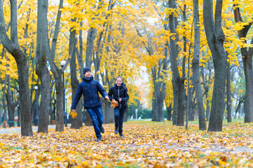 teen girl and boy running through the park and enjoys autumn, beautiful nature with yellow leaves