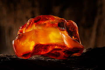 Beauty of natural raw amber. A piece of yellow-red transparent natural amber on piece of stoned wood