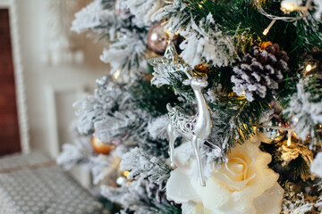 Christmas decorations in white and golden color on the branches of fir. Decorated Christmas tree with cones, deer on blurred, sparkling and fairy background. New year concept