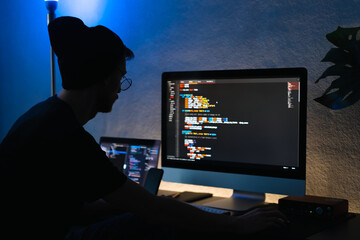 Young man mobile developer writes program code on a computer, programmer work in home office.