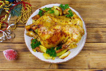 Baked whole chicken with potato and Christmas decorations on a wooden table. Top view
