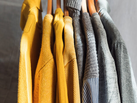 Yellow illuminated color and gray winter sweaters on wooden hangers. Trendy fashion autumn warm and cozy clothes.
