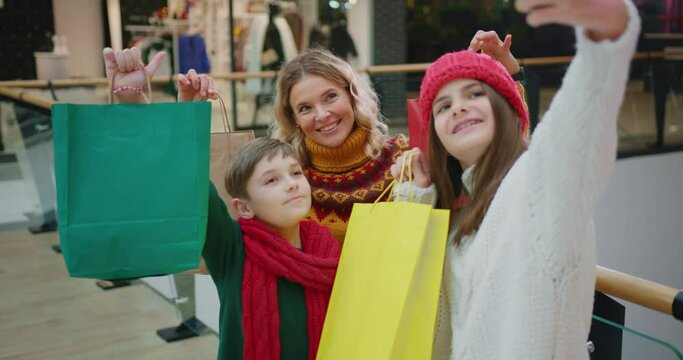 Happy caucasian mom with two joyful teenage kids taking funny selfie picture on smartphone with shopping bags. Excitement. Christmas holiday shopping. Family.