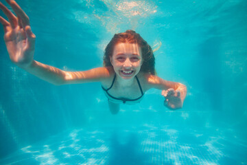 Happy little girl portrait posing underwater gesturing smile in the pool