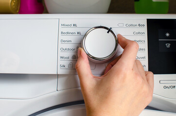 Hand turning the knob of the tumble dryer to adjust the temperature.