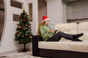 girl in a santa hat opens Christmas presents under the tree.